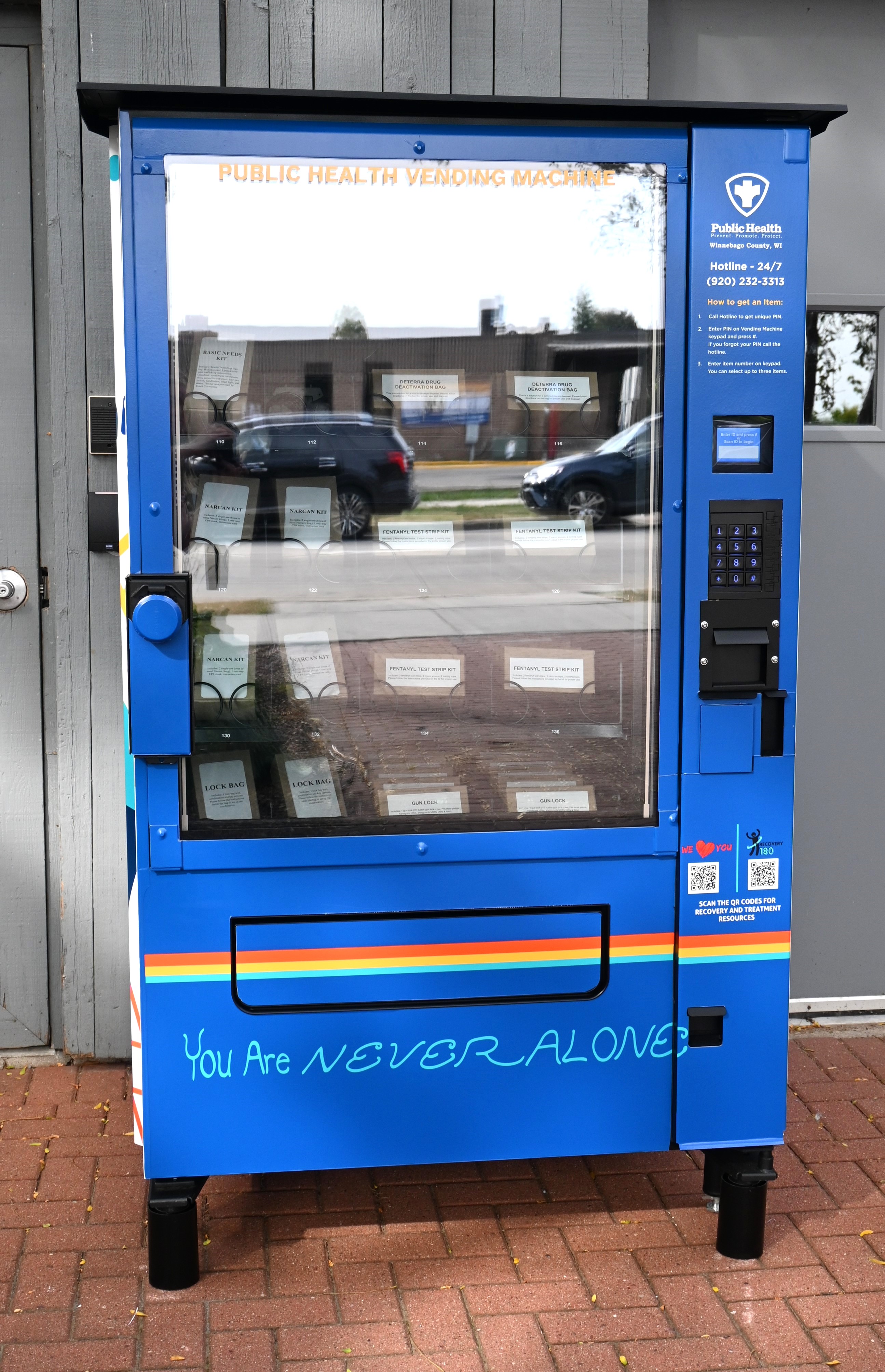 Front of the public health vending machine with the words "you are never alone" along the bottom.